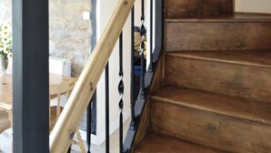 A wooden staircase with black metal railings, leading to a room with a stone wall and a wooden table with flowers.