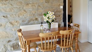A dining table with four wooden chairs, a vase with white flowers, and a bottle of wine.