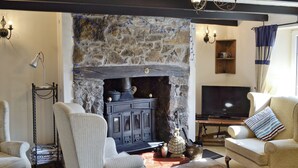 A cozy living room with a stone fireplace, comfortable seating, a television, and a bookshelf.