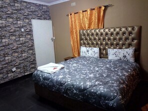 A bedroom with a stone wall, a tufted headboard, floral bedding, and an orange curtain.