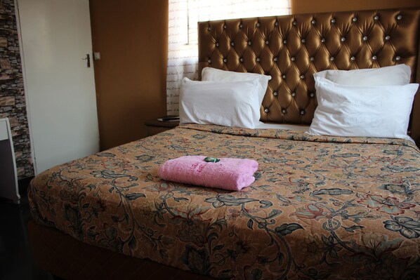 A neatly made bed with a floral-patterned bedspread, a tufted headboard, and two white pillows.