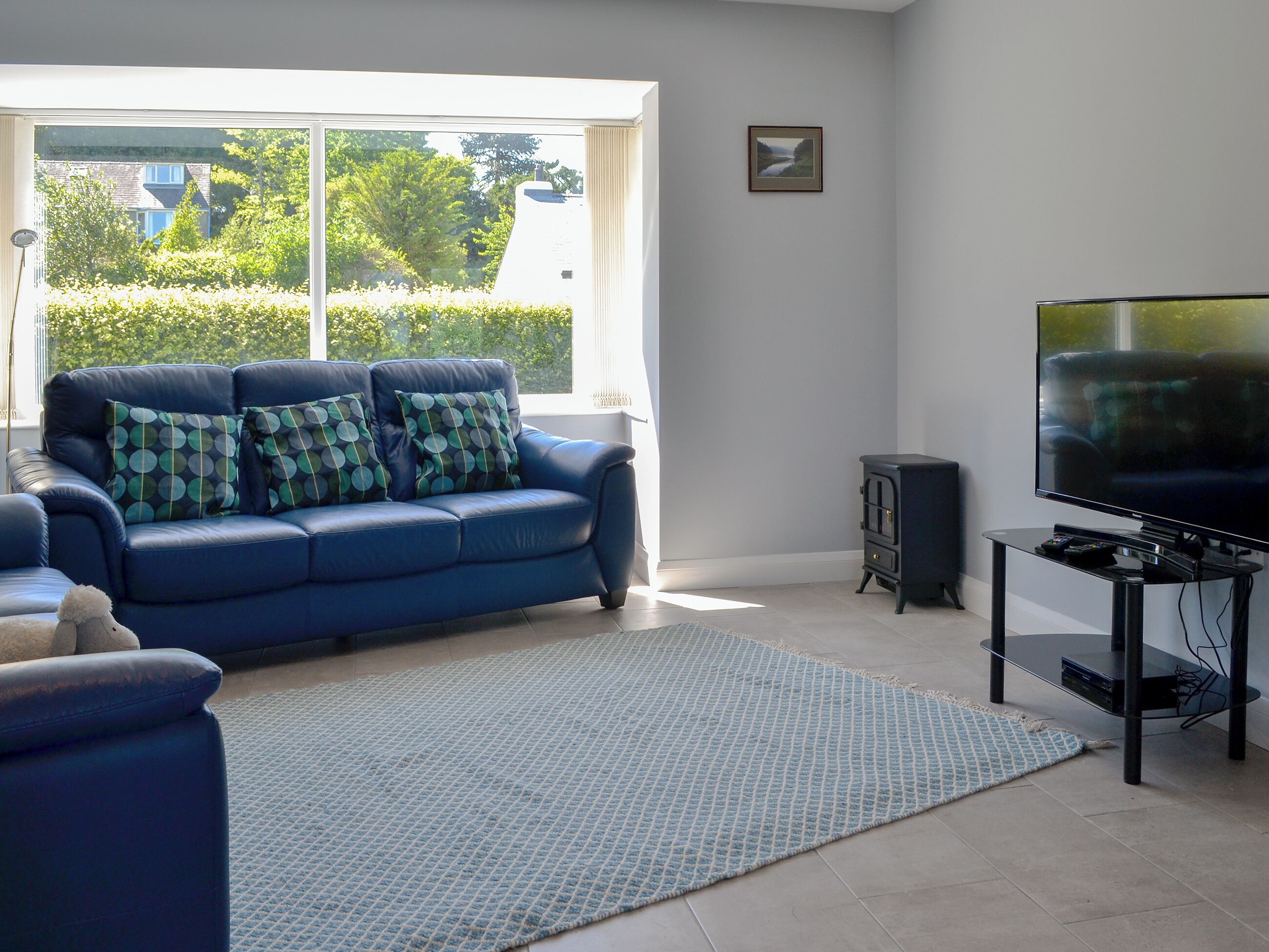 Een woonkamer met een blauwe bank, een vloerkleed, een televisie en een open haard.