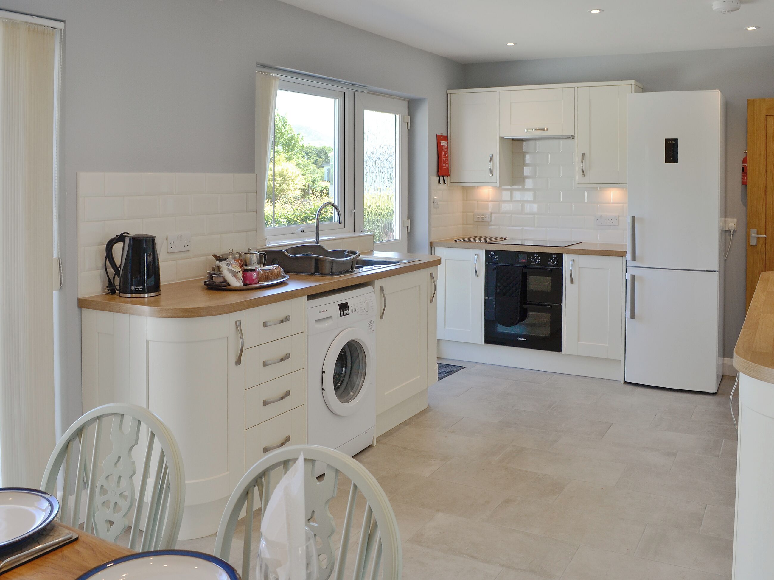 A modern kitchen with white cabinetry, a built-in oven, a dishwasher, and a washing machine.