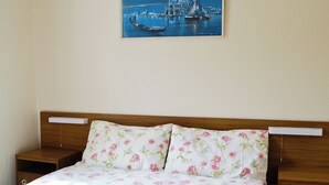 Een slaapkamer met een houten hoofdbord, bloemenbeddengoed en een schilderij van een kustlandschap boven het bed.