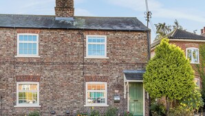 A brick house with three windows, a green door, and a small garden with flowers. - 2 bedroom accommodation in Wheldrake, near York (Wheldrake, near York)