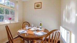 A dining room with a round wooden table set for four, surrounded by wooden chairs. A window with a view of greenery is on the left, and a radiator is on the right. - 2 bedroom accommodation in Wheldrake, near York (Wheldrake, near York)