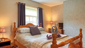 A bedroom with a wooden bed, a nightstand with a lamp, a television, and a window with curtains. - 2 bedroom accommodation in Wheldrake, near York (Wheldrake, near York)