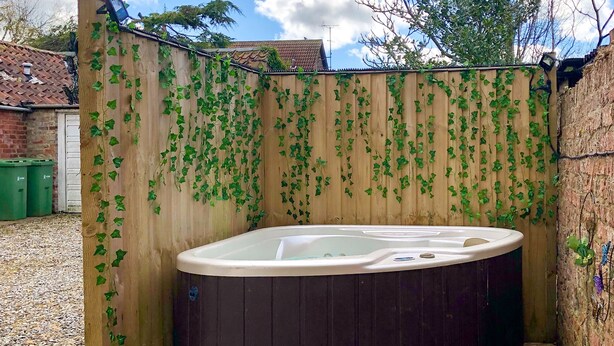 A hot tub in a wooden enclosure with a wooden deck and a brick wall. - 2 bedroom accommodation in Wheldrake, near York (Wheldrake, near York)
