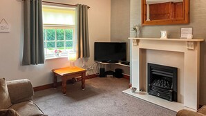 A living room with a fireplace, a television, and a window with curtains. - 2 bedroom accommodation in Wheldrake, near York (Wheldrake, near York)