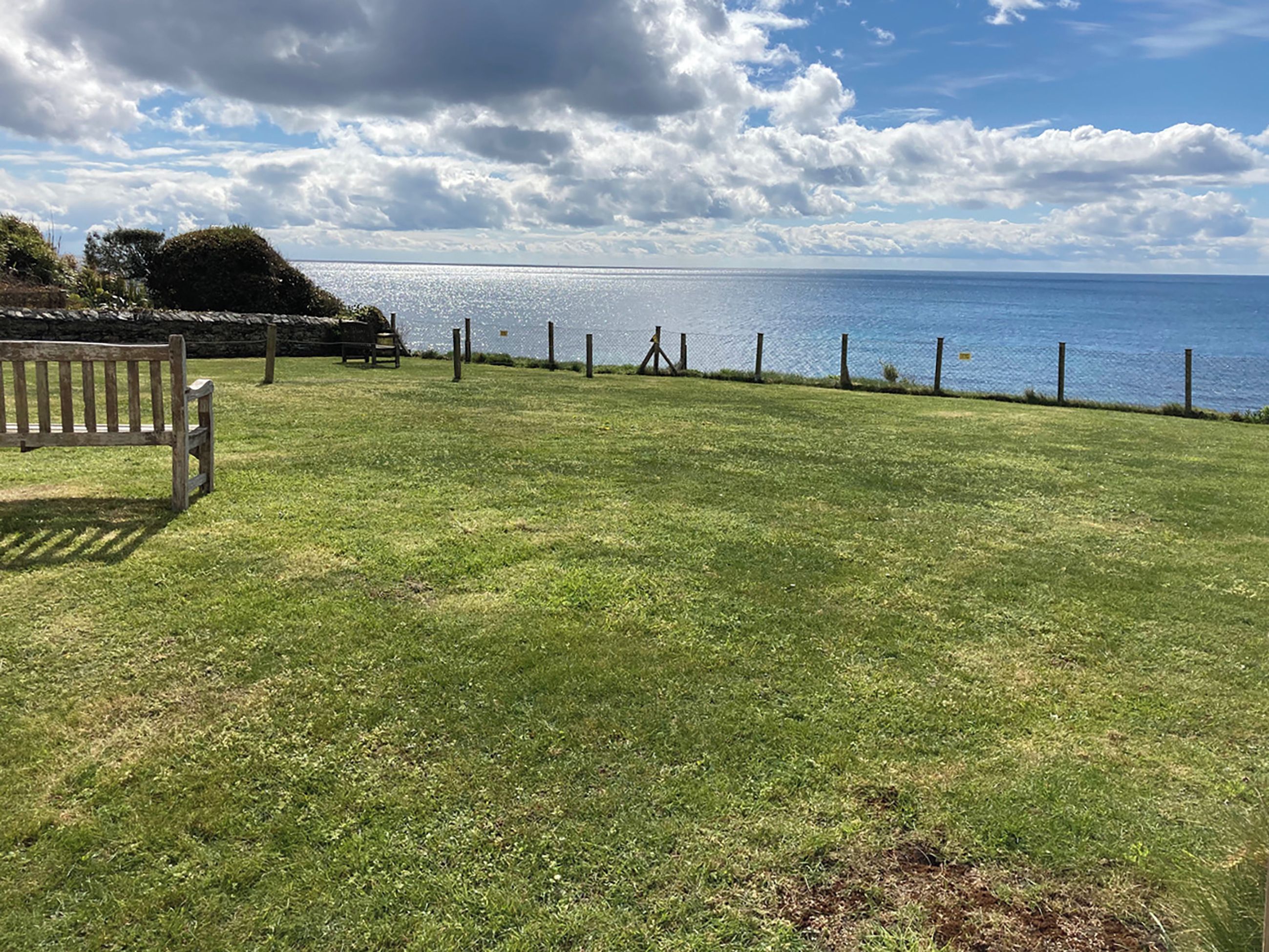 A grassy area with a bench and a fence overlooking a body of water.
