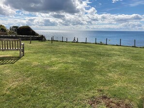 A grassy area with a bench and a fence overlooking a body of water.