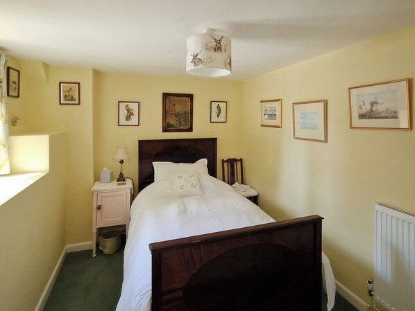 A bedroom with a bed, a nightstand, a lamp, a chair, a radiator, and several framed pictures on the walls. - 4 bedroom accommodation in Bishopstrow, near Warminster (Bishopstrow, near Warminster)