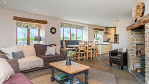 Ein geräumiger Wohnbereich mit einer Couch, einem Couchtisch und einem Kamin. Im Hintergrund befindet sich ein Esstisch mit Stühlen und eine Küchenzeile.