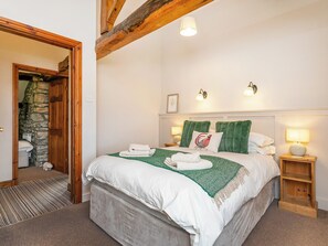 Une chambre à coucher avec un grand lit, une tête de lit en bois, deux lampes de chevet et un mur en pierre en arrière-plan.