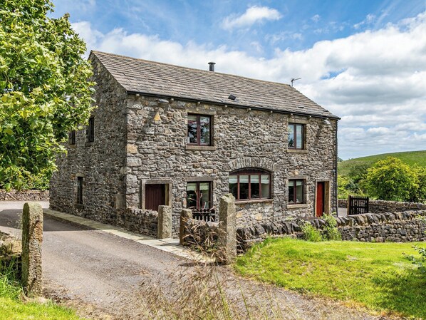 Une maison en pierre avec un toit en pente, de nombreuses fenêtres et un mur de pierre qui entoure la propriété.
