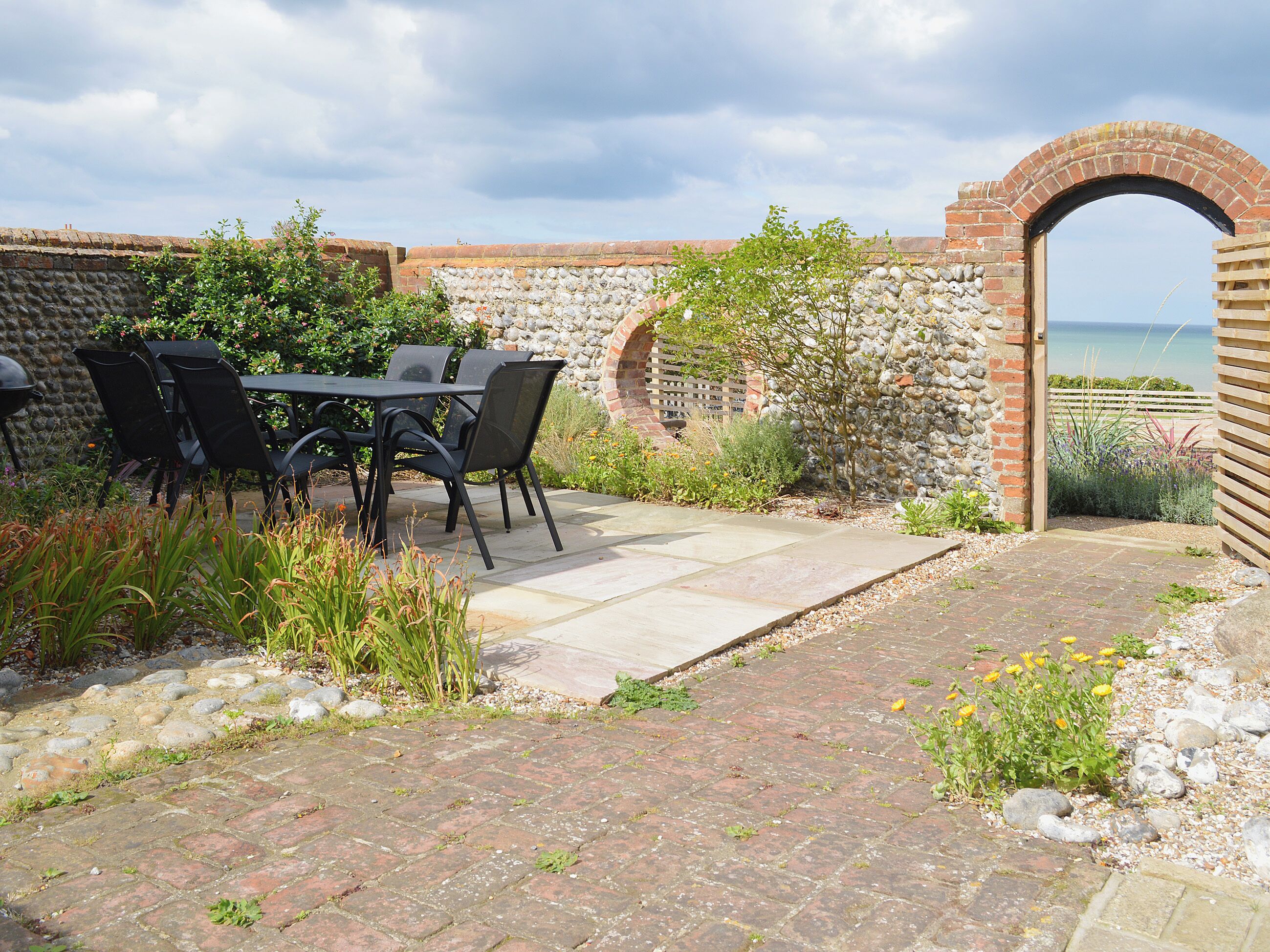 An outdoor patio with a table and chairs, a stone wall, and a view of the sea.