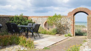 Une terrasse extérieure avec une table et des chaises, un mur en pierre et une vue sur la mer.