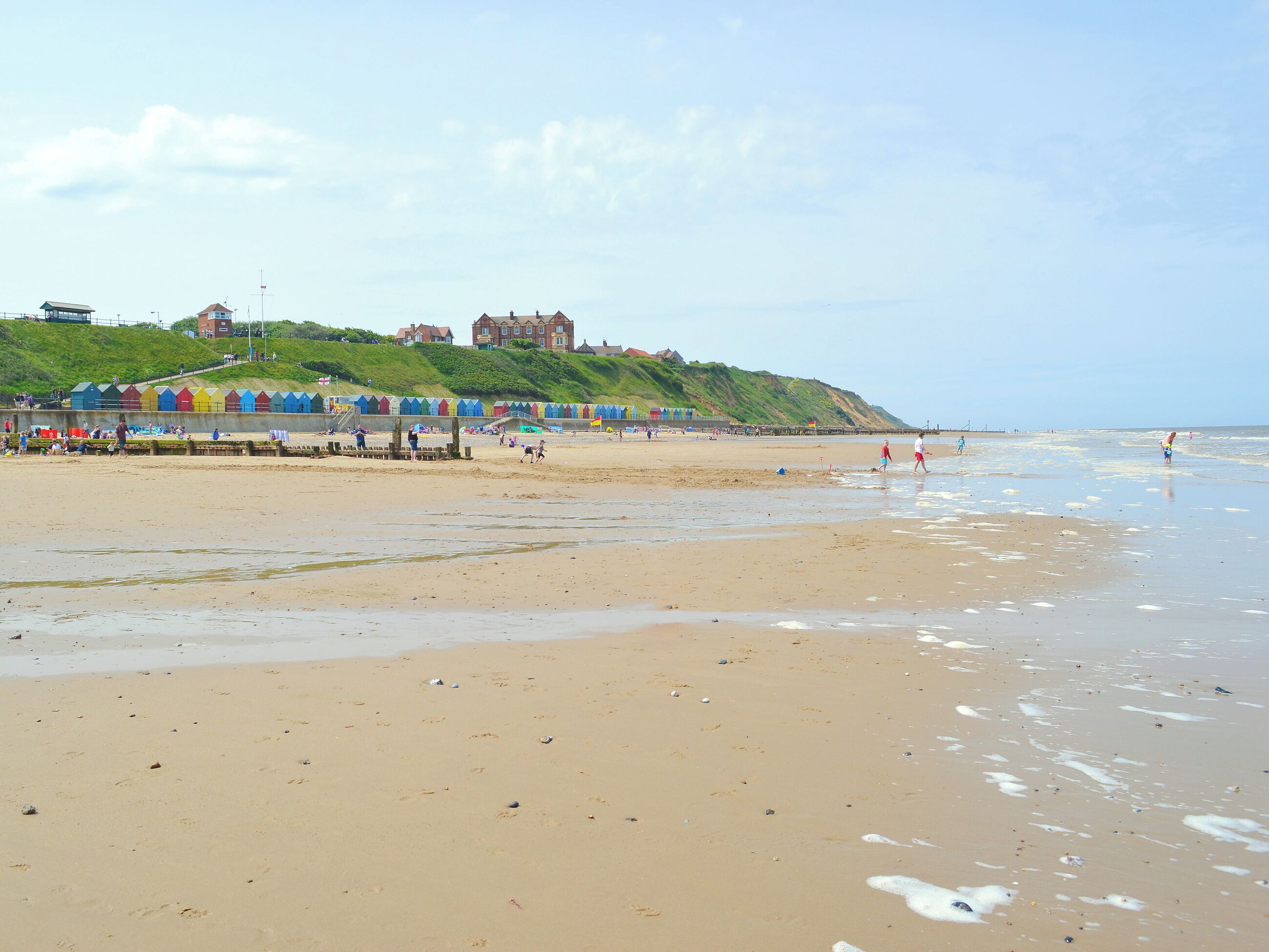 A beach with a row of colorful beach huts, a grassy hill with buildings, and the sea.