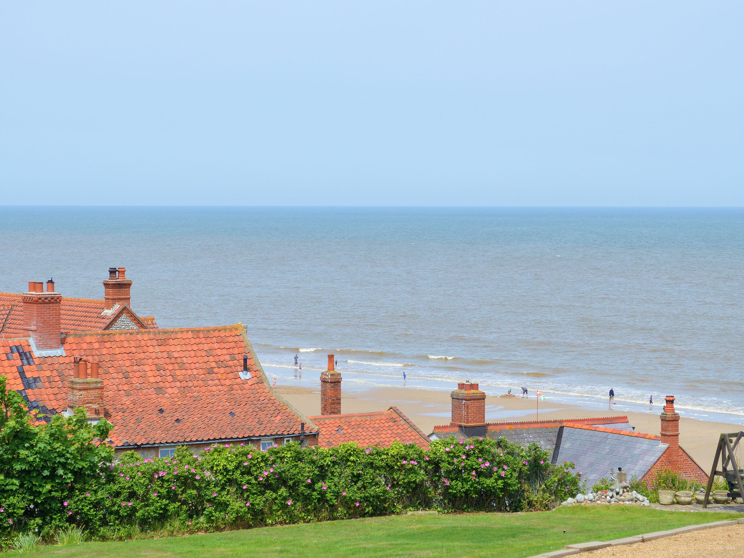A coastal view with red-roofed buildings, a sandy beach, and a clear sky.