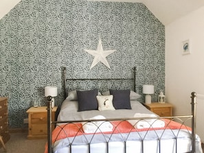 A bedroom with a patterned wallpaper, a star decoration, a bed with pillows, bedside tables, and a radiator.