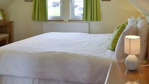 Une chambre à coucher avec un grand lit, deux fenêtres avec des rideaux verts, une lampe de chevet et un radiateur.