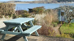 Une table de pique-nique près d’un plan d’eau, avec vue sur des collines et des maisons au loin.