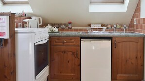 Une cuisine avec des meubles en bois, un fourneau blanc, un lave-vaisselle, un plan de travail avec des ustensiles de cuisine et des fenêtres de toit.