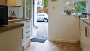 A kitchen with a clock, a car outside, and a window with plants.