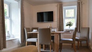 A dining area with a table, chairs, a TV mounted on the wall, and a window with curtains.