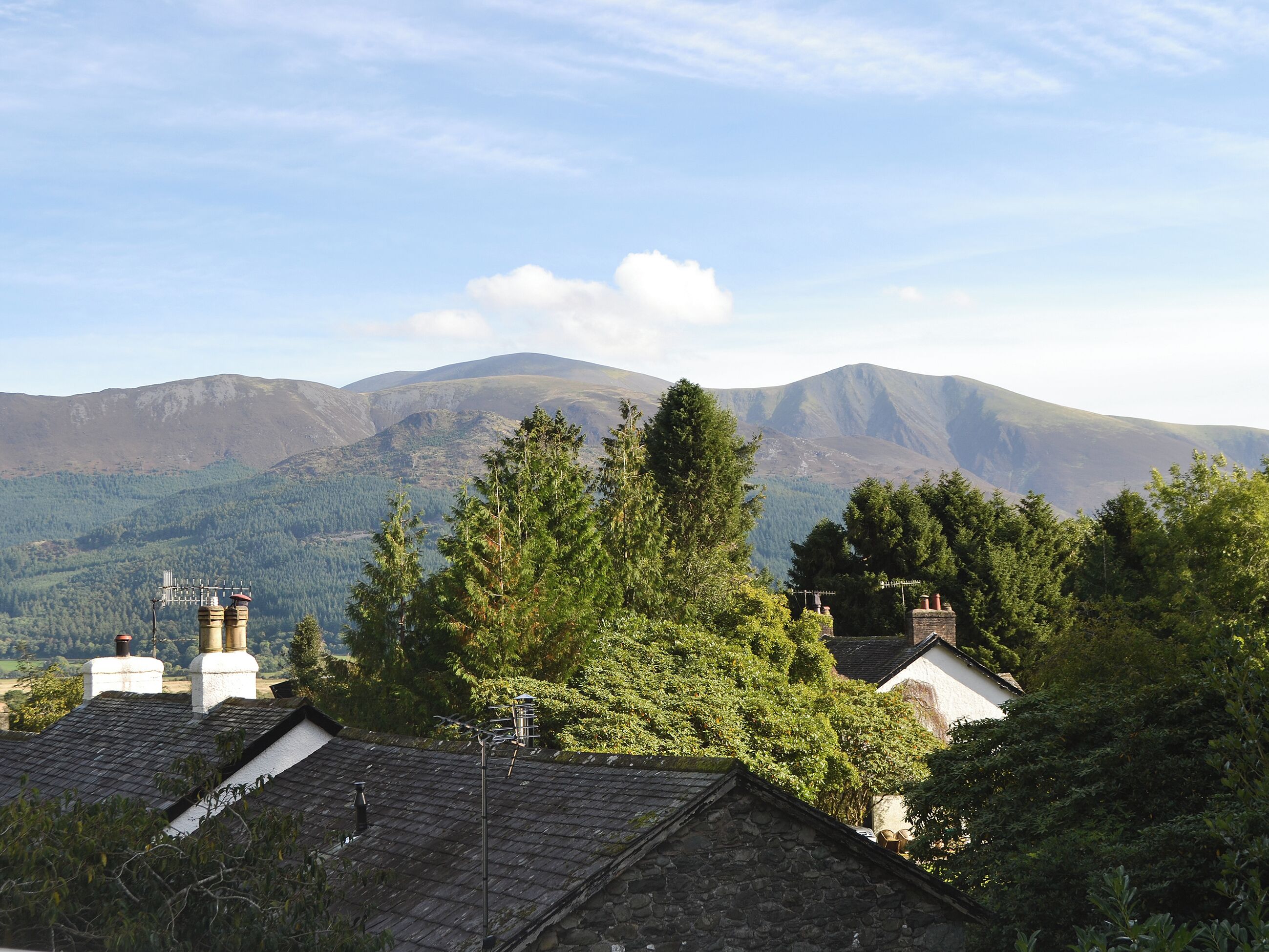 A rural landscape with mountains, trees, and traditional stone buildings.
