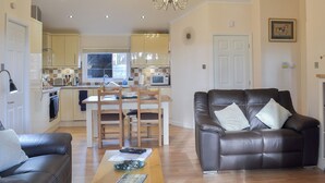 A modern living room with a leather sofa, a dining table with chairs, a kitchen in the background, and a chandelier. - 2 bedroom accommodation in Clatworthy, near Williton (Clatworthy, near Williton)