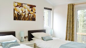 A hotel room with two beds, a window with curtains, a wall-mounted artwork, and a bedside table with a lamp. - 2 bedroom accommodation in Clatworthy, near Williton (Clatworthy, near Williton)