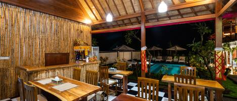Un restaurante con mobiliario de madera y una zona de piscina visible al exterior.