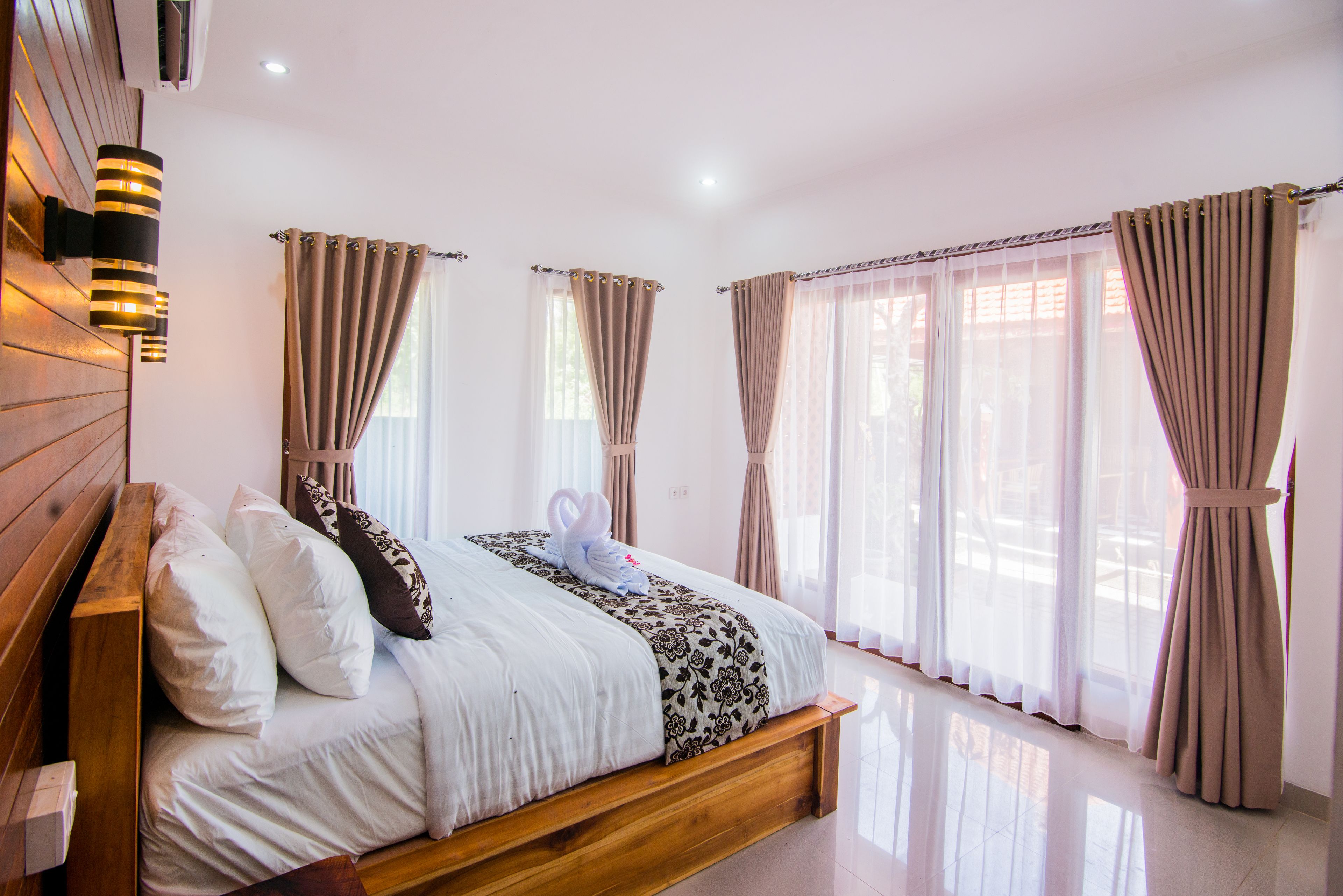 Una camera da letto con un letto di legno, tende color beige e un soffitto bianco.