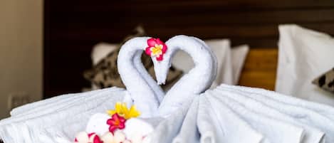 A neatly folded towel with a heart shape and a flower, placed on a bed.