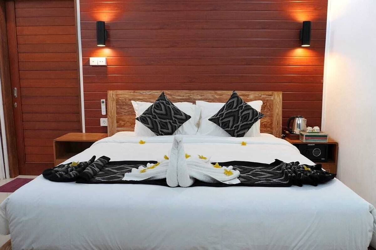 Una cama bien hecha con sábanas blancas, dos almohadas y una decoración de toallas.