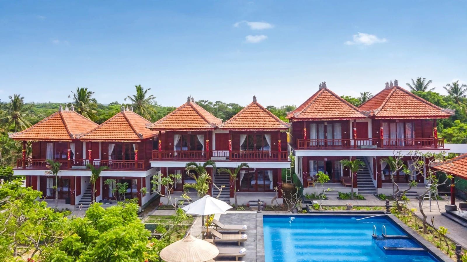 A resort with multiple red-roofed buildings, a swimming pool, and lush greenery.