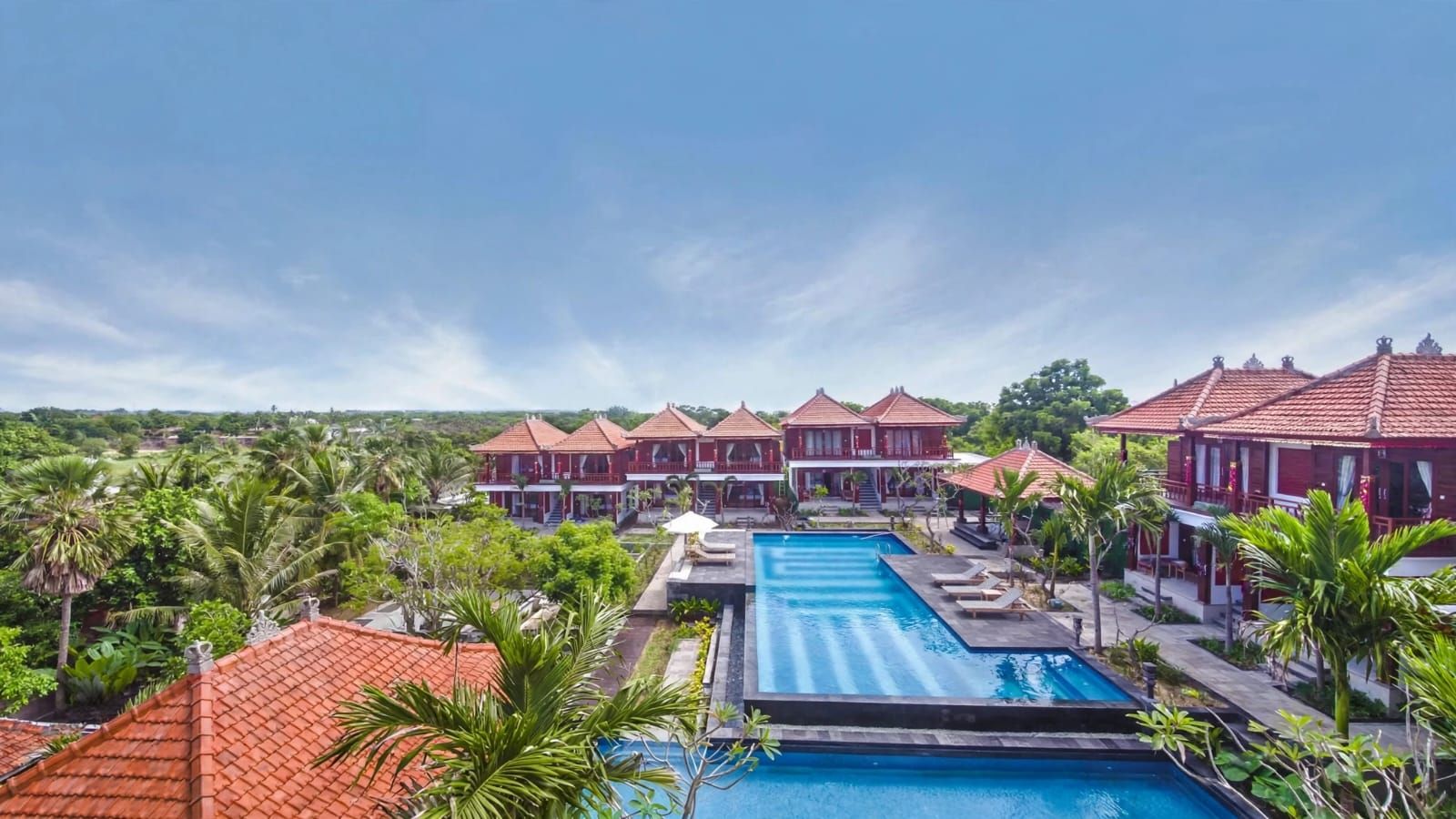 A resort with multiple red-roofed villas, a central swimming pool, and lush greenery.