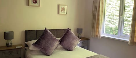 A neatly made bed with two pillows, a bedside table with a lamp, and a window with curtains.