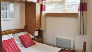 Ein Schlafzimmer mit einem Holzschrank, einem Bett mit rot-weißer Bettwäsche, einem Nachttisch mit Lampe und einem Fenster mit Jalousien und Vorhängen.