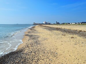 Uma praia com pedras e areia, céu claro e edifícios ao fundo.