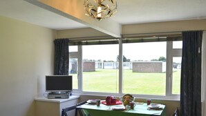 Ein Zimmer mit Schreibtisch, Stuhl, Tisch mit grüner Tischdecke und einem Fenster mit Vorhängen.