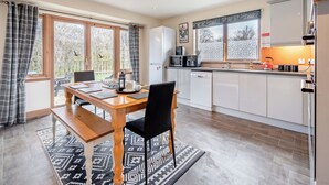 A modern kitchen with a dining area, featuring a wooden table, black chairs, and a patterned rug.