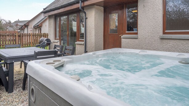 A hot tub in a backyard with a wooden deck and outdoor furniture.
