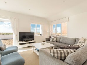 Una sala de estar moderna con televisor de pantalla plana, un sofá, una mesa de centro y una ventana con vista a la playa.