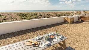 Ein Tisch mit Tellern, Gläsern und Besteck auf einer Holzterrasse mit Blick auf einen Strand.