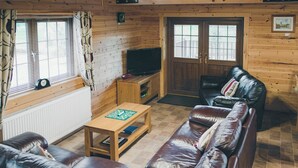 Ein gemütliches Blockhaus-Interieur mit Ledersofa, Holztisch, Fernseher und einer Tür mit Fenstern.