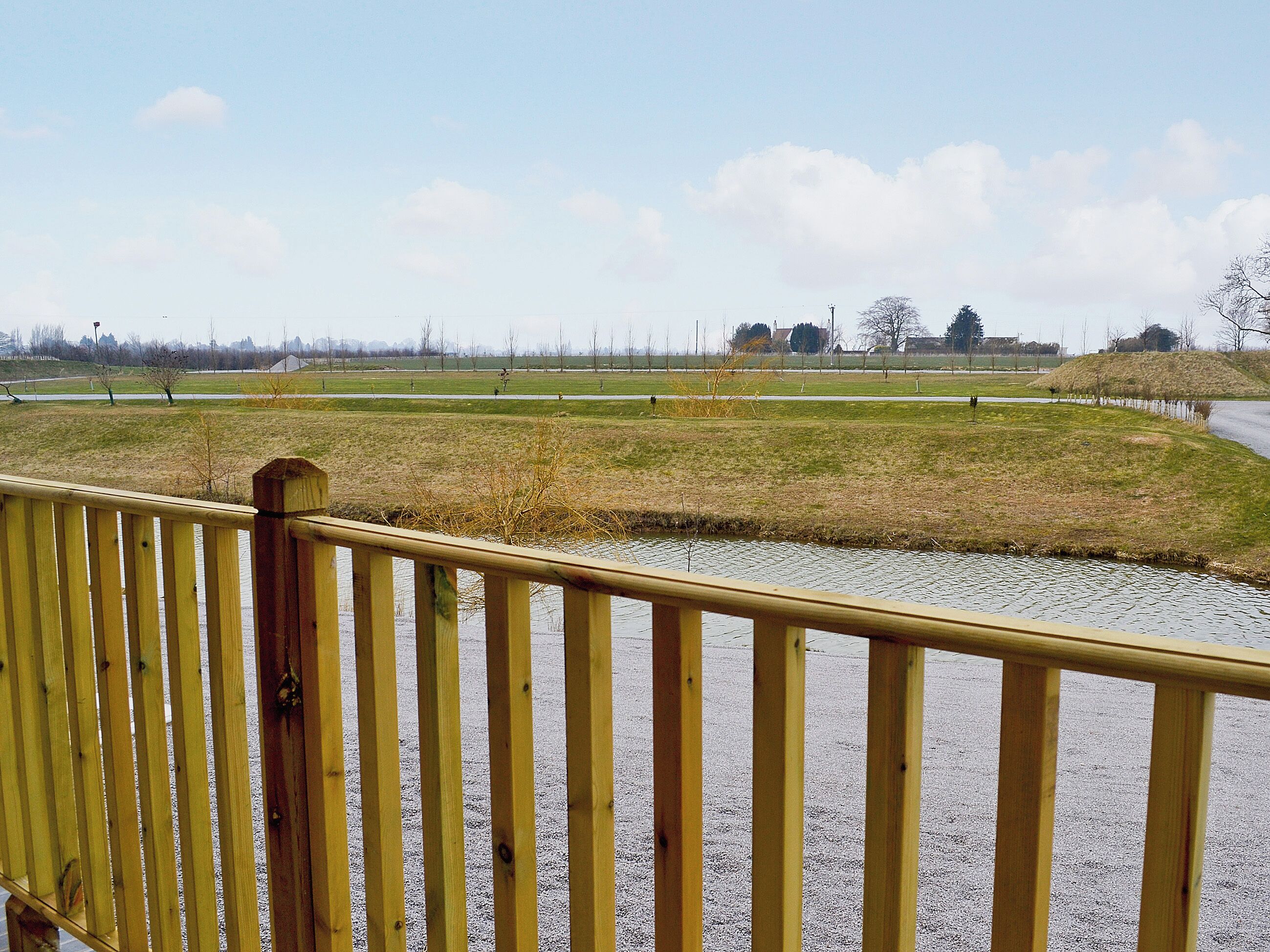 Eine Holzterrasse mit Blick auf ein grasbewachsenes Feld und ein Gewässer.