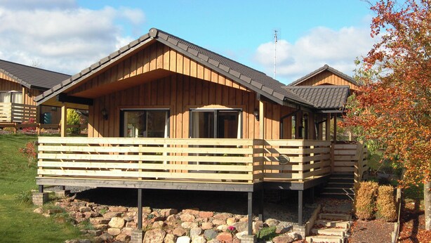 Une cabane en bois dotée d’un balcon, de grandes fenêtres et de fondations en pierre.