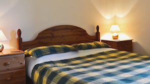 A bed with a plaid bedspread, a wooden headboard, a nightstand with a lamp, and a drawer. - 2 bedroom accommodation in Portree (Portree)